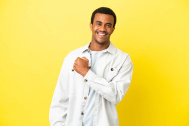 Afro-Amerikalı yakışıklı adam sarı arka planda zaferi kutluyor.