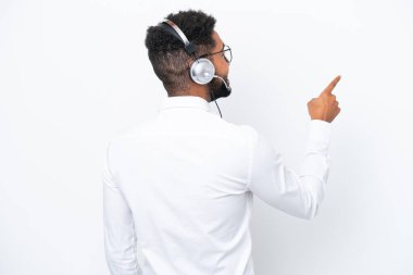 Telemarketer Brazilian man working with a headset isolated on white background pointing back with the index finger