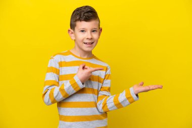 Sarı arka planda izole edilmiş küçük beyaz çocuk bir ilan vermek için avucunun içinde hayali bir mekan tutuyor.