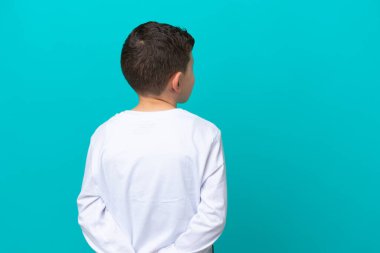 Küçük çocuk mavi arka planda izole edilmiş. Arka planda ve geriye bakıyor.