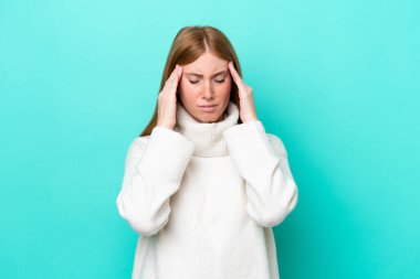 Genç kızıl saçlı kadın mavi arka planda baş ağrısı ile izole edilmiş.