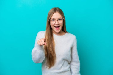 Mavi arka planda izole edilmiş genç Rus kadın şaşırmış ve ön tarafı işaret ediyor.