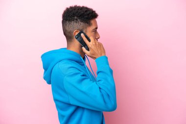 Pembe arka planda izole edilmiş genç Brezilyalı bir adam cep telefonuyla sohbet ediyor.
