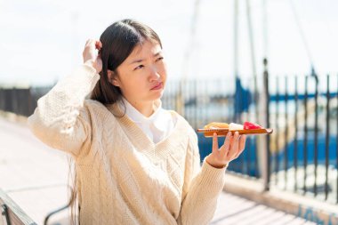 Genç Çinli kadın açık havada sashimi tutuyor şüpheleri var ve kafası karışmış bir yüz ifadesi var.