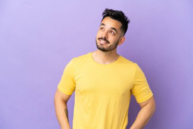 Kafkasyalı genç bir adam mor arka planda izole edilmiş, yukarı bakarken bir fikir düşünüyor.