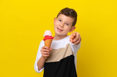 Sarı arka planda izole edilmiş kornet dondurması olan beyaz çocuk mutlu bir ifadeyle önü işaret ediyor.