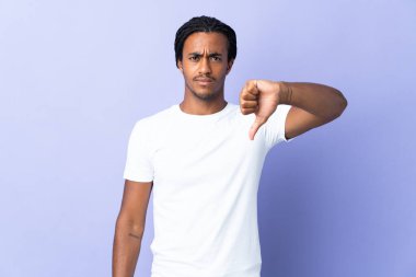 Örgülü genç Afro-Amerikalı adam, mor arka planda izole edilmiş, olumsuz bir ifadeyle baş parmağını gösteriyor.