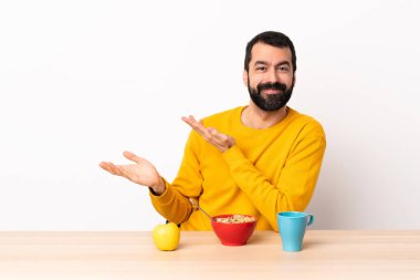 Beyaz bir adam kahvaltısını bir masada yapıyor. Davet edildiği için ellerini yana açıyor..