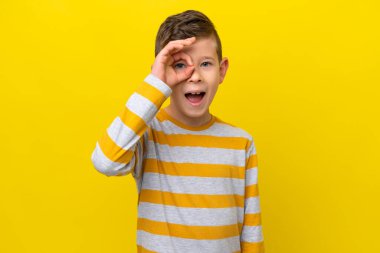 Sarı arka planda izole edilmiş küçük beyaz çocuk parmaklarıyla tamam işareti gösteriyor.