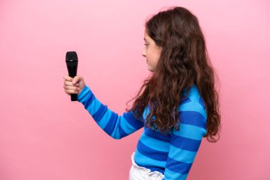 Küçük şarkıcı kız pembe arka planda izole edilmiş neşeli bir mikrofonu kaldırıyor.