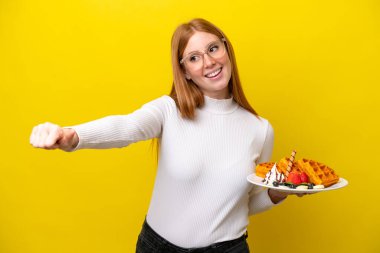 Sarı arka planda gözleme tutan genç kızıl saçlı kadın işaret veriyor.