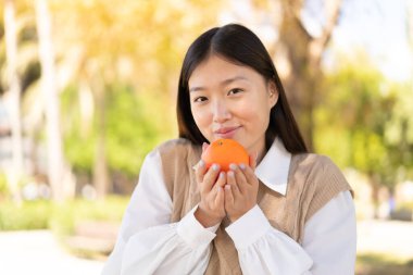 Açık havada elinde portakal tutan güzel bir Çinli kadın.