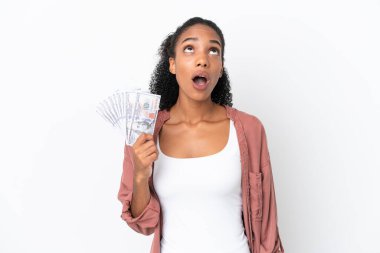 Genç Afrikalı Amerikalı bir kadın beyaz arka planda izole edilmiş bir sürü para alıyor yukarı bakıyor ve şaşırmış bir ifadeyle
