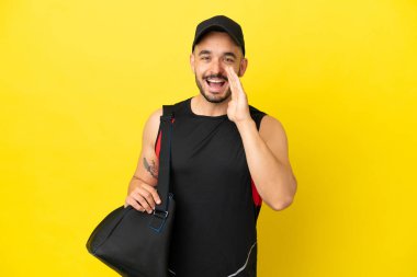 Spor çantalı genç beyaz adam sarı arka planda izole edilmiş ağzı açık bağırıyor.