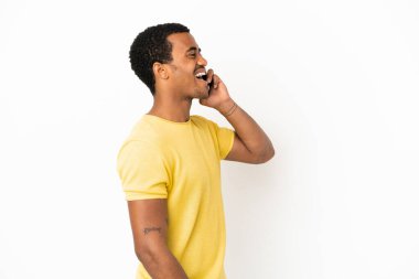 Beyaz arka planda cep telefonu kullanan Afro-Amerikalı yakışıklı adam yan pozisyonda gülüyor.