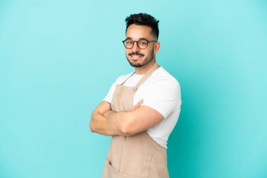 Restoran garsonu Kafkasyalı adam mavi arka planda izole edilmiş, kolları bağlı ve ileriye bakıyor.