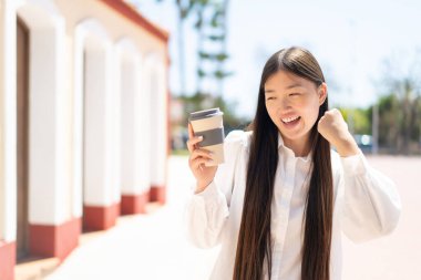 Güzel Çinli kadın açık havada kahvesini yudumluyor ve zaferi kutluyor.