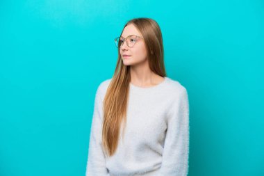 Mavi arka planda izole edilmiş genç Rus kadın yan tarafa bakıyor.