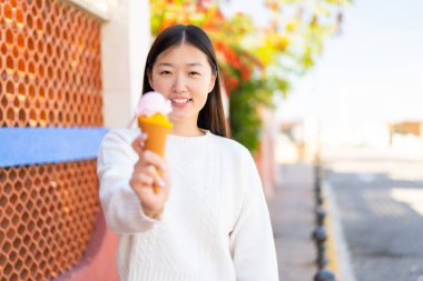 Açık havada kornet dondurmalı güzel bir Çinli kadın, neşeli bir ifadeyle.