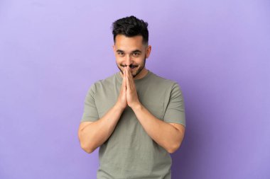 Mor arka planda izole edilmiş genç beyaz adam avuç içlerini bir arada tutuyor. İnsan bir şey ister.