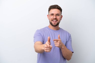 Beyaz arka planda izole edilmiş genç beyaz adam ön tarafı işaret ediyor ve gülümsüyor.