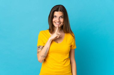 Mavi arka planda izole edilmiş genç Slovak kadın parmağını ağzına koyan sessizlik işareti gösteriyor.