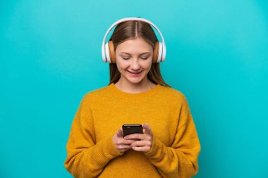 Genç Rus kadın mavi arka planda izole edilmiş müzik dinliyor ve cep telefonu arıyor.
