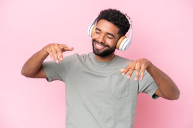 Genç Brezilyalı adam pembe arka planda izole edilmiş müzik ve dans dinliyor.