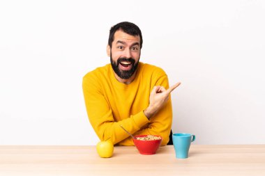 Masada kahvaltı yapan beyaz bir adam şaşırmış ve işaret ediyor..