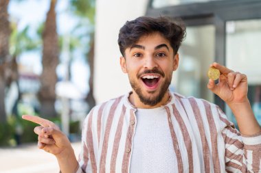 Açık havada Bitcoin tutan yakışıklı bir Arap şaşırdı ve parmağını yana çevirdi.