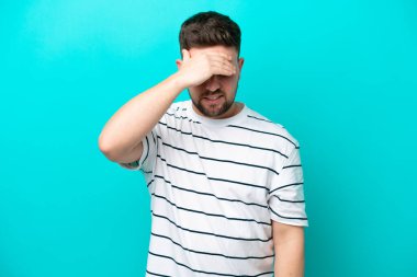 Kafkasyalı genç adam mavi arka planda izole edilmiş, baş ağrısı var.
