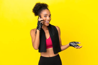 Genç Afrikalı sporcu kadın sarı arka planda izole edilmiş cep telefonuyla biriyle sohbet ediyor.