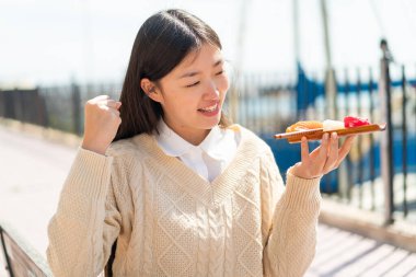 Genç Çinli kadın açık havada saşimi tutuyor ve zaferi kutluyor.