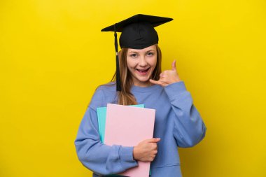 Sarı arka planda izole edilmiş genç bir Rus öğrenci telefon jesti yapıyor. Bana geri dönüş işareti ver.