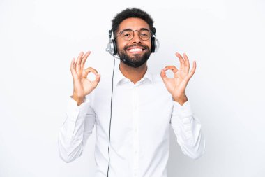 Telemarketer Brazilian man working with a headset isolated on white background showing an ok sign with fingers