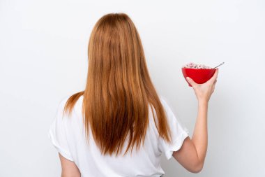 Genç kızıl saçlı kadın arka planda beyaz arka planda bir kase mısır gevreği tutuyor.