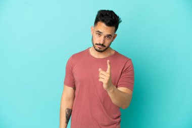 Mavi arka planda izole edilmiş genç beyaz adam hayal kırıklığına uğramış ve ön tarafı işaret ediyor.