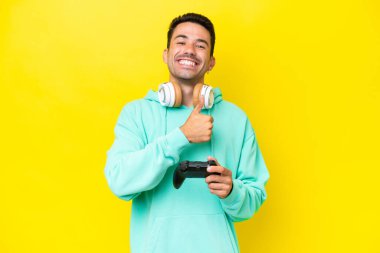 Genç yakışıklı bir adam, izole edilmiş duvarın üzerinde bilgisayar oyunu kontrolörüyle oynuyor ve baş parmak işareti yapıyor.