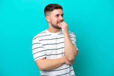 Mavi arka planda izole edilmiş genç beyaz adam biraz gergin.