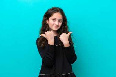 Mavi arka planda izole edilmiş küçük bir kız başparmakları havada ve gülümsüyor.
