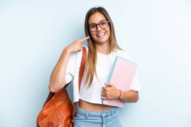 Mavi arka planda izole edilmiş genç bir bayan baş parmak hareketi yapıyor.