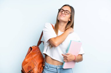 Genç bayan öğrenci, mavi arka planda izole edilmiş, omuz ağrısı çekiyor, çabaladığı için.