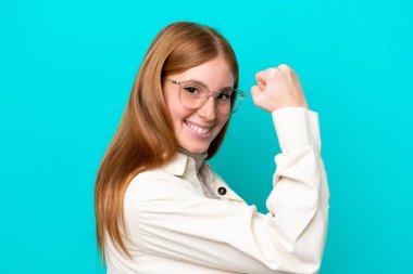 Mavi arka planda, gözlüklü ve zaferi kutlayan genç kızıl saçlı kadın.