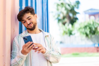 Yakışıklı bir Arap açık havada üzgün bir ifadeyle cep telefonu kullanıyor.