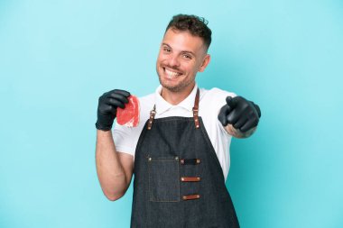 Kasap beyaz adam önlük giyer ve mavi arka planda izole edilmiş taze et servis eder.