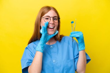 Genç kızıl saçlı dişçi kadın sarı arka planda izole edilmiş ve ağzı açık bağırıyor.