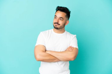 Mavi arka planda izole edilmiş genç beyaz adam yan tarafa bakıyor.