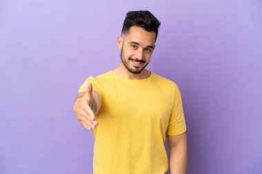 Mor arka planda izole edilmiş genç beyaz adam iyi bir anlaşma için el sıkışıyor.