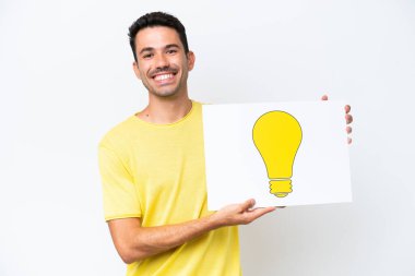 İzole edilmiş beyaz arka plan üzerinde genç yakışıklı bir adam elinde mutlu ifadeli bir ampul simgesi olan bir levha tutuyor.