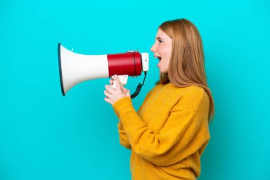 Genç kızıl saçlı kadın mavi arka planda izole edilmiş bir şekilde megafonla bir şey duyurmak için bağırıyor.